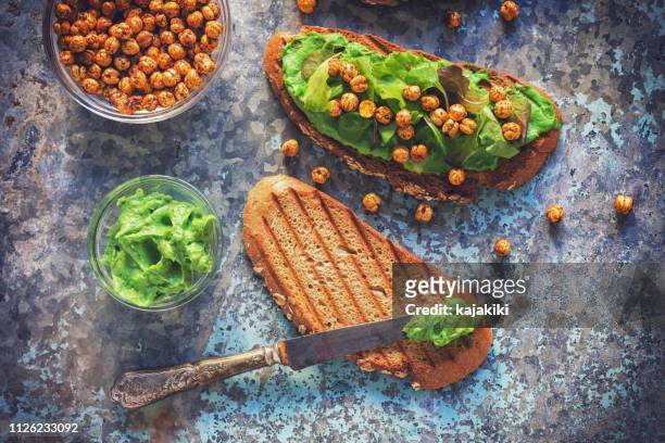 avocado toast gegarneerd met hummus, slaatje en krokant geroosterde kikkererwten - avocado toast stockfoto's en -beelden