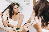 Hair and body care. Young happy woman in white towel applying conditioner mask on hair in bathroom, mirror reflection. Slim sexy woman with natural skin enjoying spa and wellness, relaxing