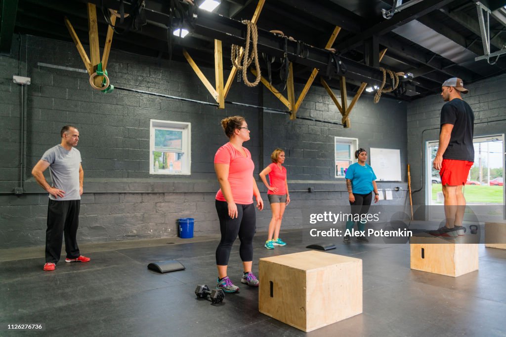 El joven entrenador masculino demostrando como hacer squats en el cubo al grupo de las mujeres en el gimnasio