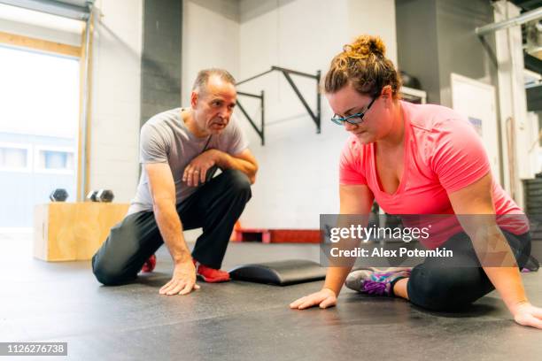 de jonge, lichaam-positieve kaukasische vrouw doen uitrekkende training onder toezicht van de senior, 55-jaar-oud, mannelijke latino-coach. - 55 years old white man active stockfoto's en -beelden