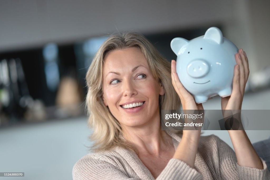 Glückliche Frau zu Hause halten ein Sparschwein mit ihren Ersparnissen