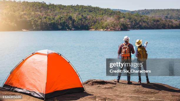 young couple hikers with backpacks enjoying view looking at on top of the mountain landscape valley lake view, camping, vacation and travel concept - young men camping stock pictures, royalty-free photos & images