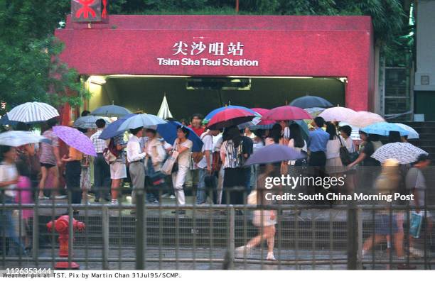 Crowds of people dating friends at the destination of the Tsim Sha Tsui MTR Station in a rainy day.