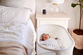 Three month old baby asleep in his cot beside the bed in his motherâ