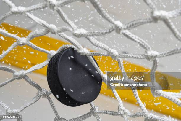 primo piano di un disco da hockey su ghiaccio che colpisce la parte posteriore della rete mentre la neve vola, vista frontale - hockey su ghiaccio foto e immagini stock