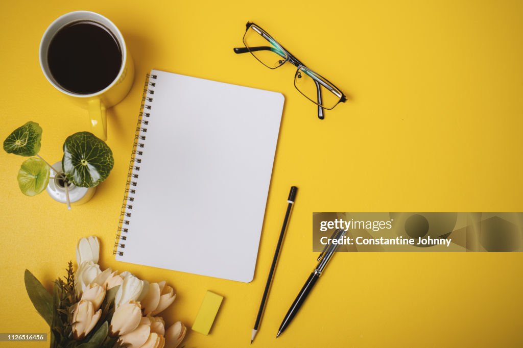 Blank Notepad Page, Coffee Mug, Pen and Flower on Yellow Background.