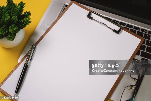 clipboard with blank white paper on laptop over yellow background. - clipboard and glasses stock pictures, royalty-free photos & images