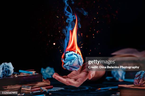 fire on a crumpled paper ball in a writer workplace with drafts, papers, books, and pencils. creative block concept. dark background with copy space - burns stock-fotos und bilder