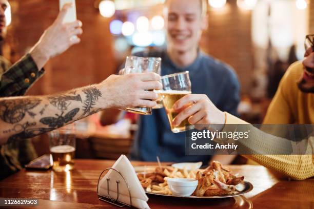 close up of male friends toasting with beer in a cafe - chicken wings stock pictures, royalty-free photos & images