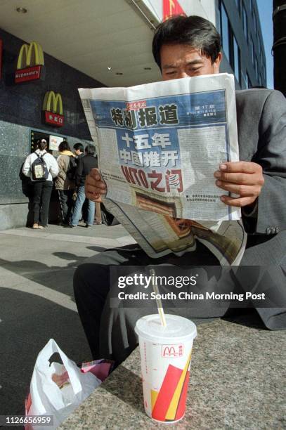 Beijing resident reads a local newspaper with a story about China's admission to the World Trade Organisation outside a McDonald's restaurant in the...