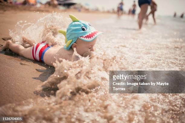 baby boy surprised by a wave while playing at the seashore - baby playing stock-fotos und bilder
