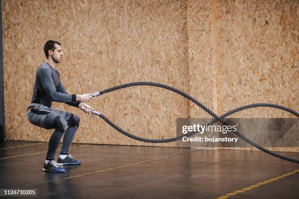 man working out with battle ropes at a gym - battle rope stock pictures, royalty-free photos & images