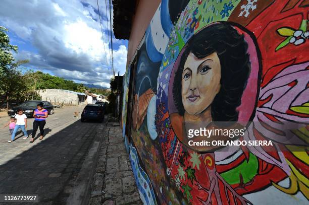 Woman with her children pass on February 22, 2019 near a mural depicting slain Honduran environmental Berta Caceres, in the Honduran municipality of...
