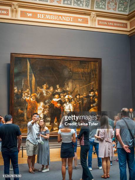 Tourist observing The Night Watch, a painting by Rembrandt Harmenszoon van Rijn, at the Rijksmuseum in Amsterdam, The Netherlands. Rembrandt is...