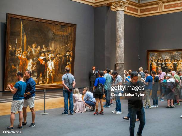 Tourist looking at The Night Watch, a painting by Rembrandt Harmenszoon van Rijn, at the Rijksmuseum in Amsterdam, The Netherlands. Rembrandt is...