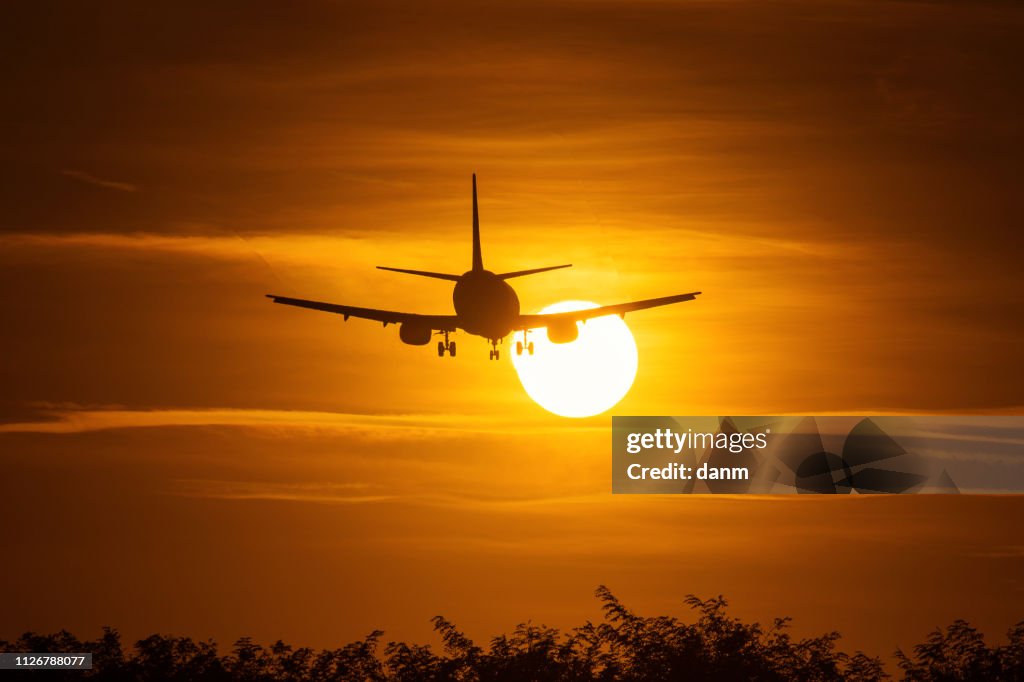 Silhouette of an air plane over the sun with beautiful red clouds in background