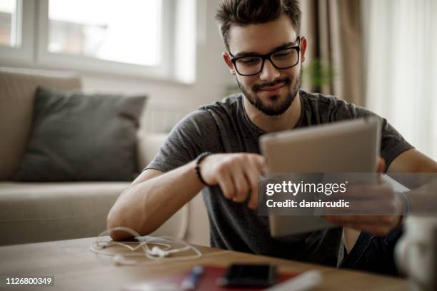 hombre joven con tableta digital en el hogar - buscador fotografías e imágenes de stock