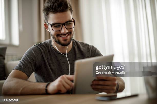 lächelnder junge mann mit digital-tablette zu hause - young boy enjoying music stock-fotos und bilder