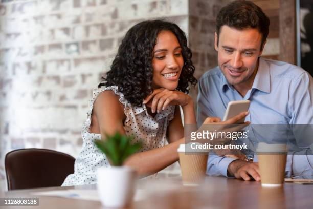 businessman and businesswoman looking at a mobile phone. - sharing coffee stock pictures, royalty-free photos & images