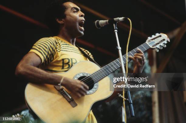 Gilberto Gil, Brazilian singer-songwriter and guitarist, singing into a microphone while playing the guitar during a live concert performance, circa...