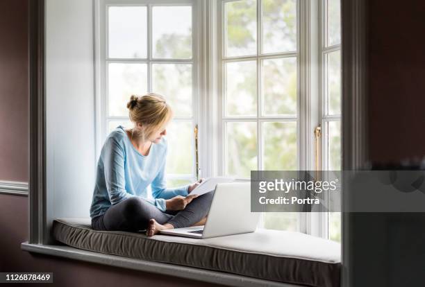 vrouw met laptop schrijven op papier thuis - window seat stockfoto's en -beelden