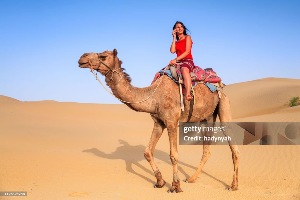 Junge weibliche Touristen mit mobile auf einem Kamel