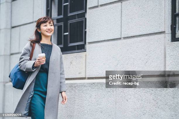 portrait of businesswoman walking in street while holding coffee - japanese woman stock pictures, royalty-free photos & images