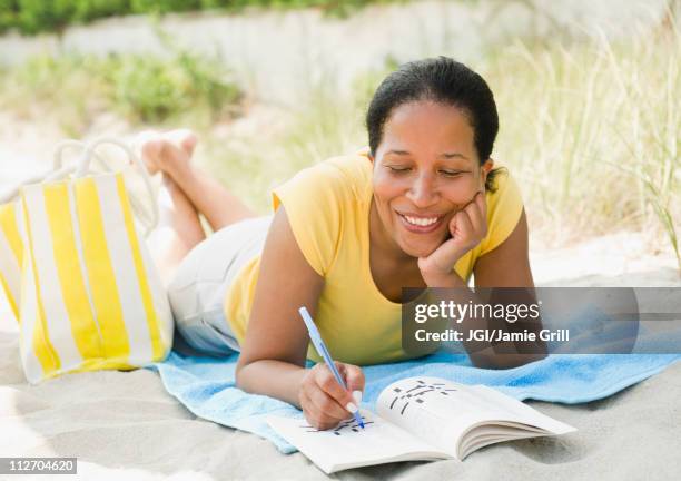 black woman doing crossword puzzle on beach - word puzzle stock pictures, royalty-free photos & images