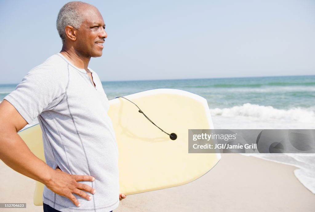 Black man holding body board on beach