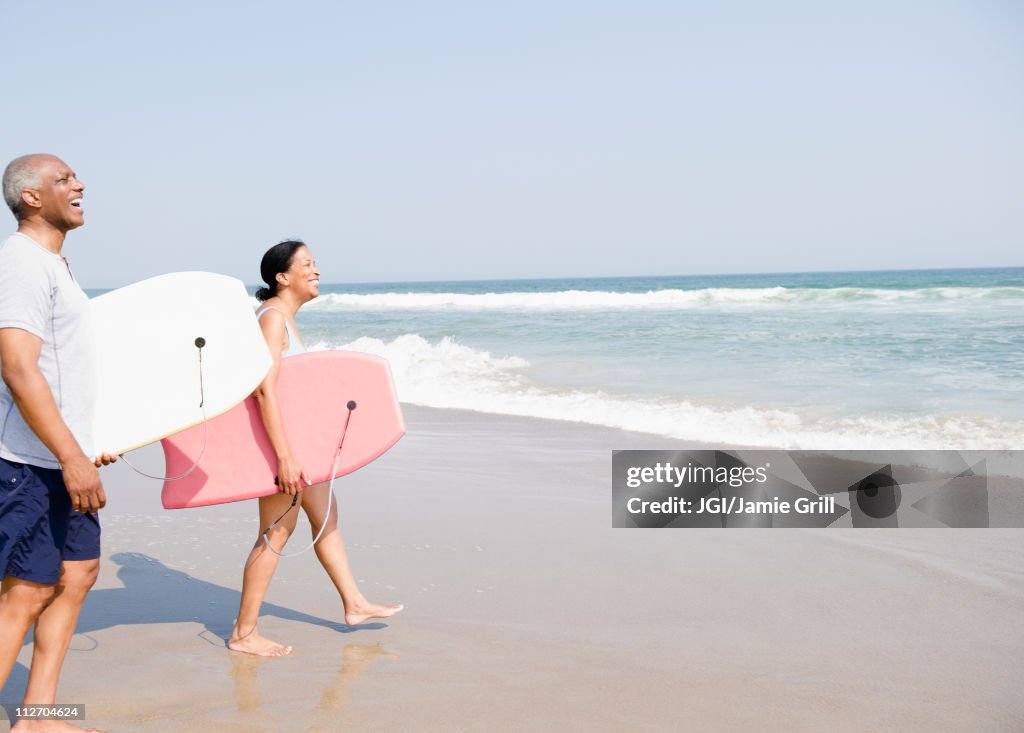 Black couple holding body boards on beach