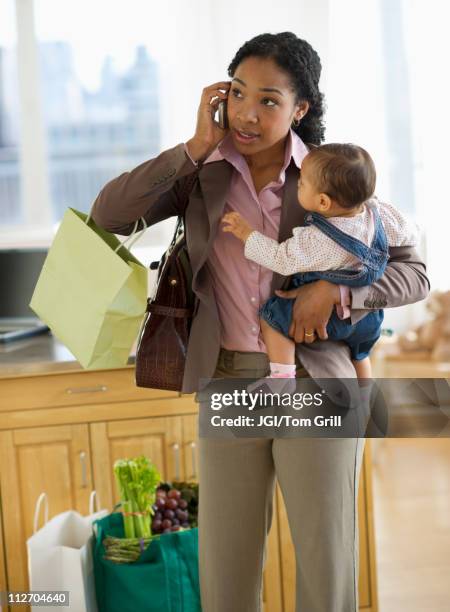 mixed race mother holding baby and talking on cell phone - working mum stock pictures, royalty-free photos & images