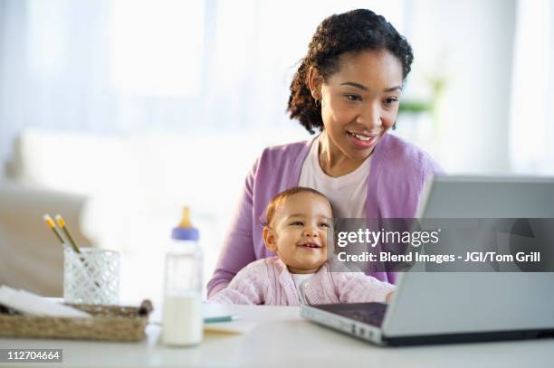 mixed race woman holding baby and using laptop - indian food bildbanksfoton och bilder