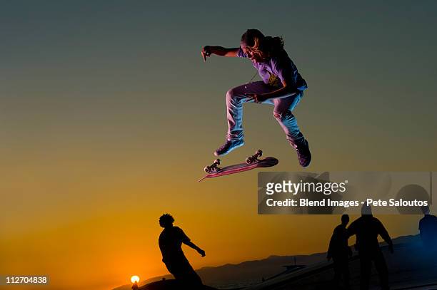 skateboarder doing stunt in mid-air at sunset - boys sunset stock-fotos und bilder