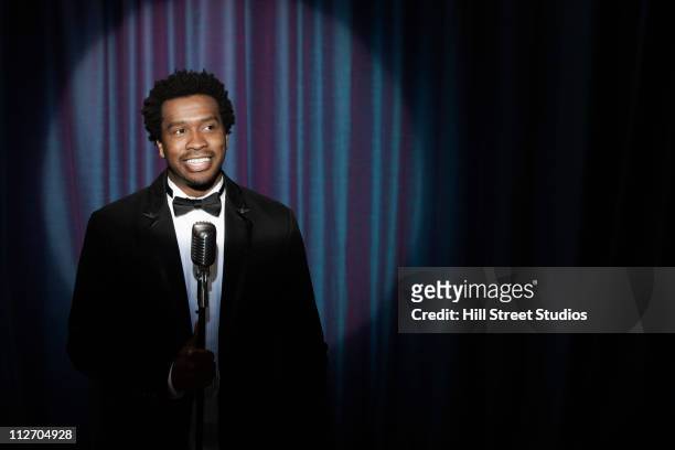 smiling black man in tuxedo standing at microphone - male singer stock pictures, royalty-free photos & images