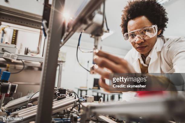 black female engineer working on industrial machine in a laboratory. - engineer stock pictures, royalty-free photos & images