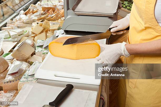 a sales clerk slicing cheese at the cheese counter - queso en forma redonda fotografías e imágenes de stock
