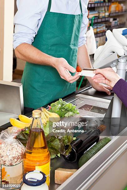 a customer handing a cashier a credit card at the supermarket - caisse photos et images de collection