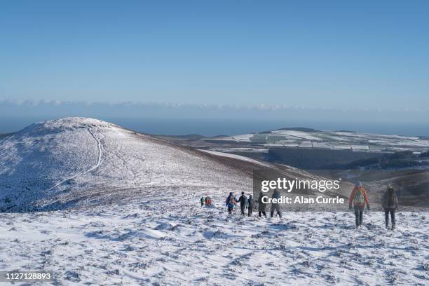 group of hikers descending mountain in deep snow across a beautiful calm scenic landscape, with blue sky on a winter day - ireland winter stock pictures, royalty-free photos & images