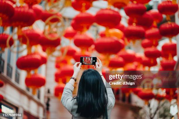 rear view of woman taking photos of traditional chinese red lanterns with smartphone on city street - chinese new year lanterns bildbanksfoton och bilder