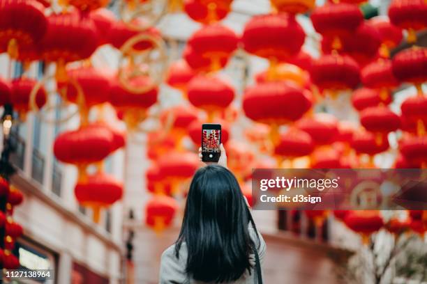 rear view of woman taking photos of traditional chinese red lanterns with smartphone on city street - 中国 提灯 ストックフォトと画像