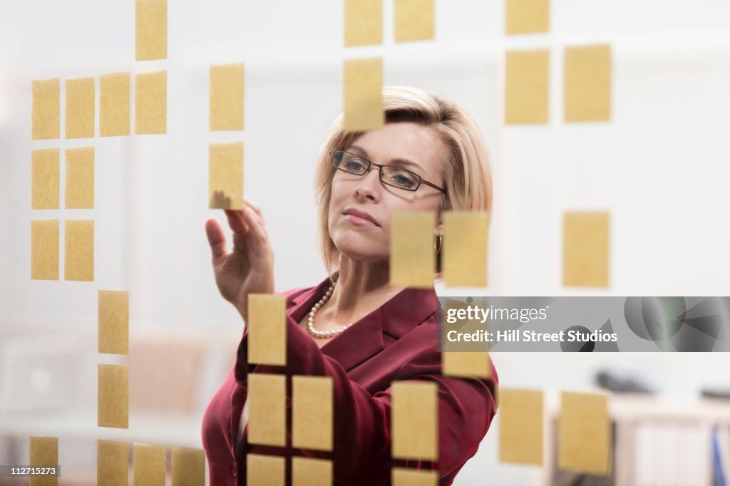 Caucasian businesswoman arranging sticky notes on wall