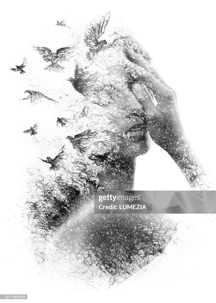 Paintography. Double Exposure portrait of an elegant woman with closed eyes combined with hand made pencil drawing of a flock of birds flying freely resembling disintegrating particles of her being