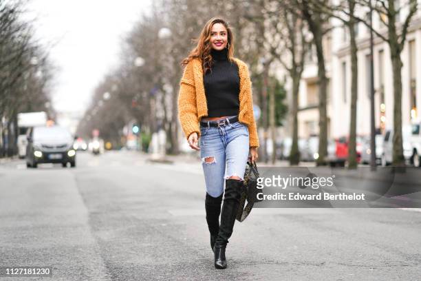 Patricia Contreras wears a Lady Dior bag, an orange knitted wool jacket, a black turtleneck top, ripped jeans, a Hermes belt, black leather thigh...