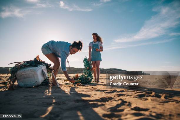 two women collecting garbage on the beach - entreprendre photos et images de collection