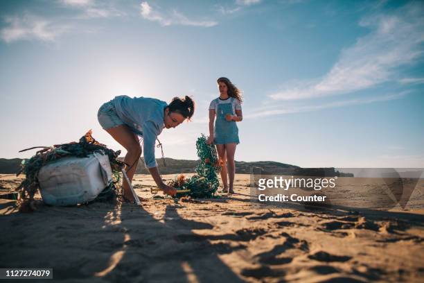 two women collecting garbage on the beach - plastic pollution beach stock pictures, royalty-free photos & images