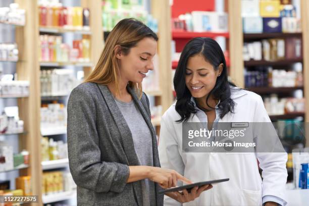 woman explaining over digital tablet to chemist - female pharmacist with a digital tablet imagens e fotografias de stock