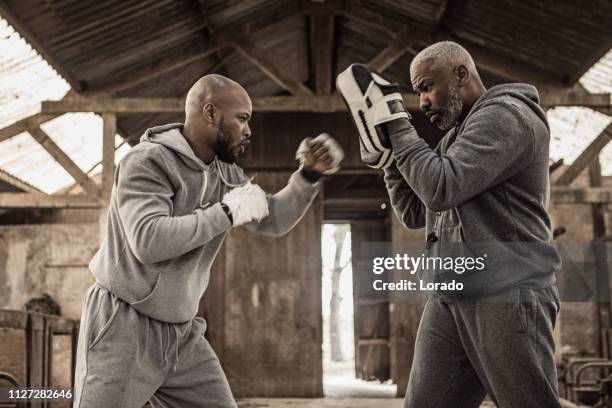 Black fighter working out with coach in an abandoned farm