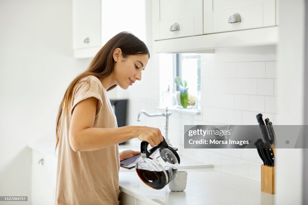 Giovane donna che versa caffè in tazza a casa