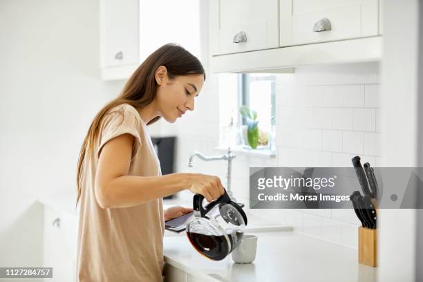 young woman pouring coffee in cup at home - coffee drink stock pictures, royalty-free photos & images