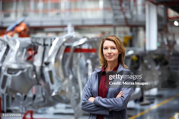 female engineer with arms crossed by car chassis - production line worker stock pictures, royalty-free photos & images